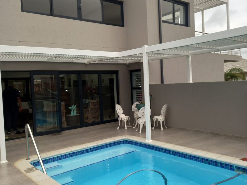 A modern outdoor pool area featuring a tiled surround, a white metal pergola, and direct access to the home through large sliding glass doors.