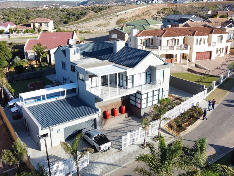 Aerial view of a modern multi-level residential property featuring a metal roof, paved driveway, swimming pool, and attached balcony and patio areas.