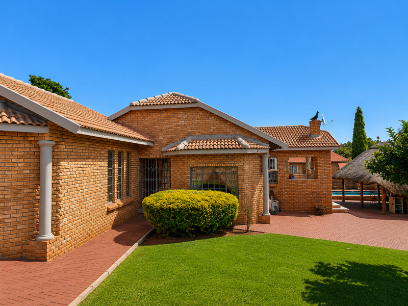 Rear view of a face brick house featuring a paved patio area, well-maintained lawn, and access to a swimming pool and thatched lapa.