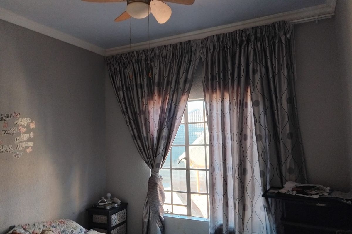 A bedroom featuring a ceiling fan, window with security bars, and decorative cornice detailing.