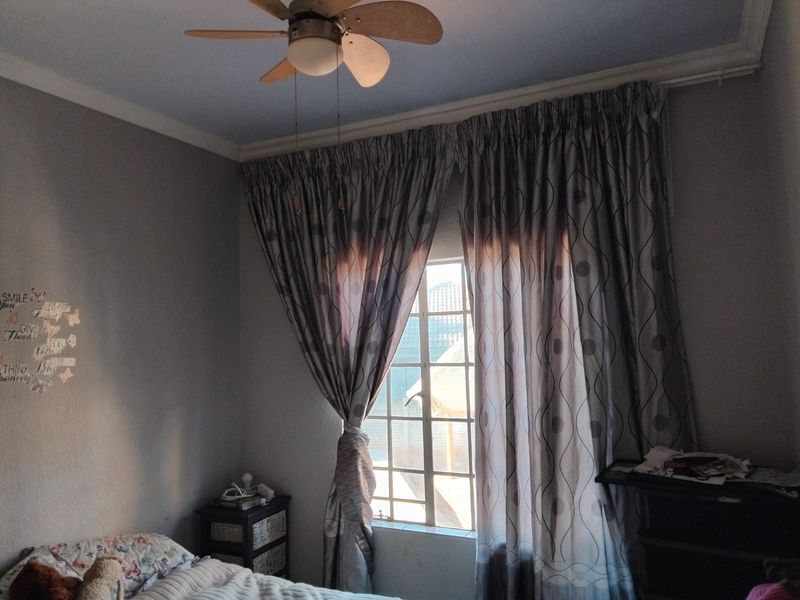 A bedroom featuring a ceiling fan, window with security bars, and decorative cornice detailing.
