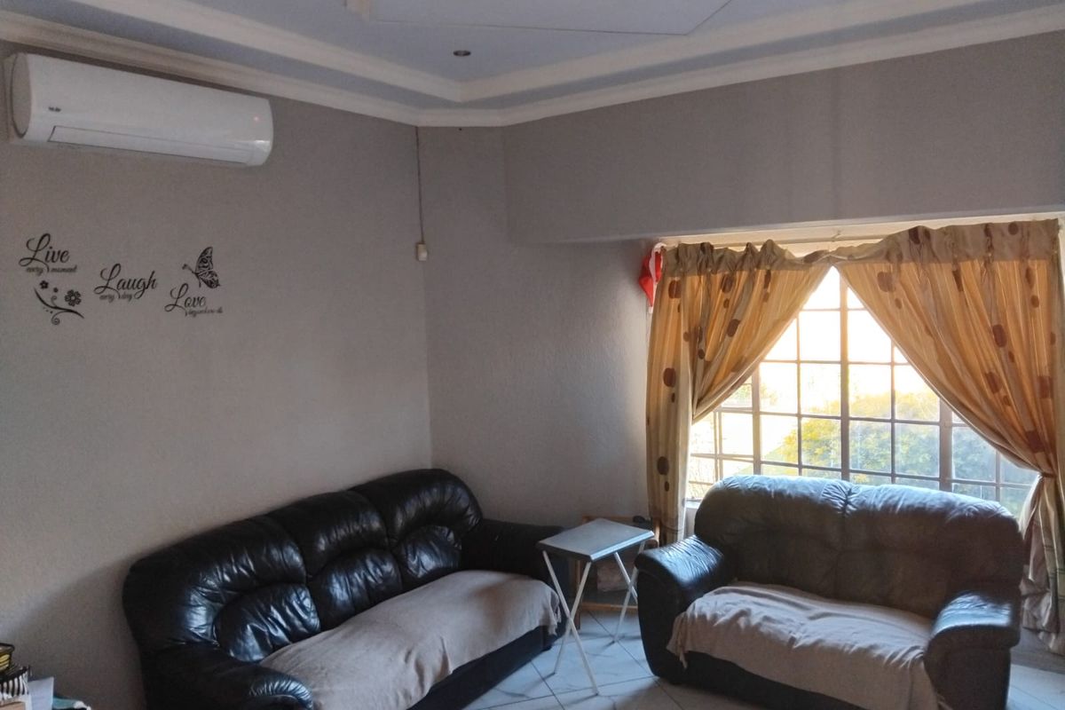 A living room featuring tiled flooring, a split-system air conditioner, and a large window with security bars, offering a functional and comfortable living space.