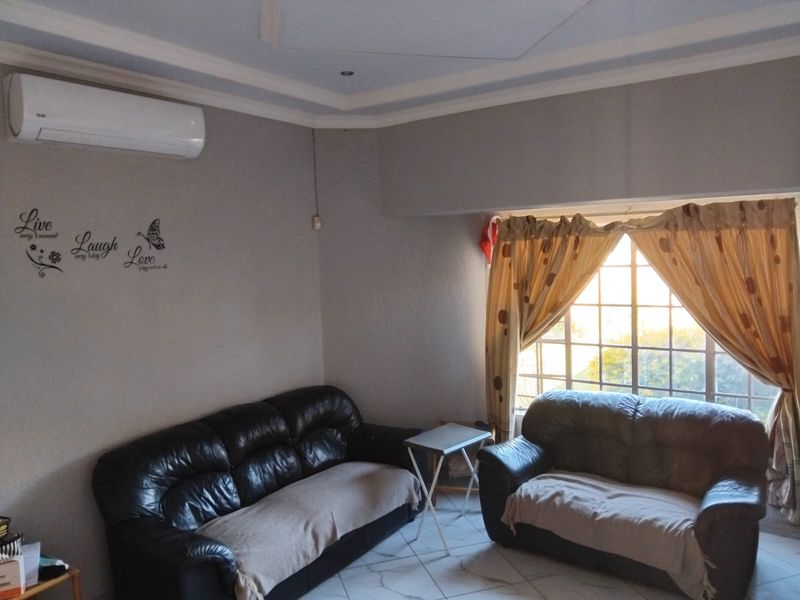 A living room featuring tiled flooring, a split-system air conditioner, and a large window with security bars, offering a functional and comfortable living space.