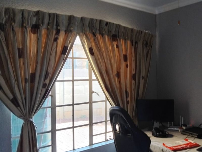 A functional home office space featuring a window with security bars and a ceiling fan, providing a quiet area for work or study.