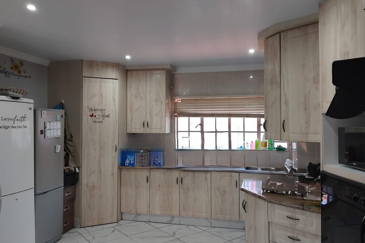 A functional kitchen featuring light wood-finish cabinetry, granite-look laminate countertops, tiled flooring, and integrated appliances with recessed ceiling lighting.
