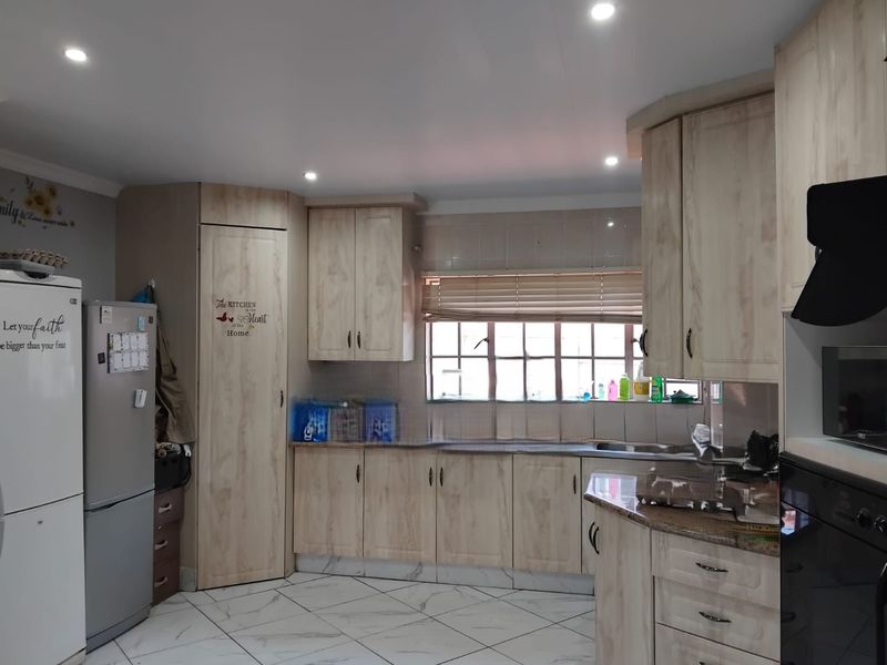 A functional kitchen featuring light wood-finish cabinetry, granite-look laminate countertops, tiled flooring, and integrated appliances with recessed ceiling lighting.