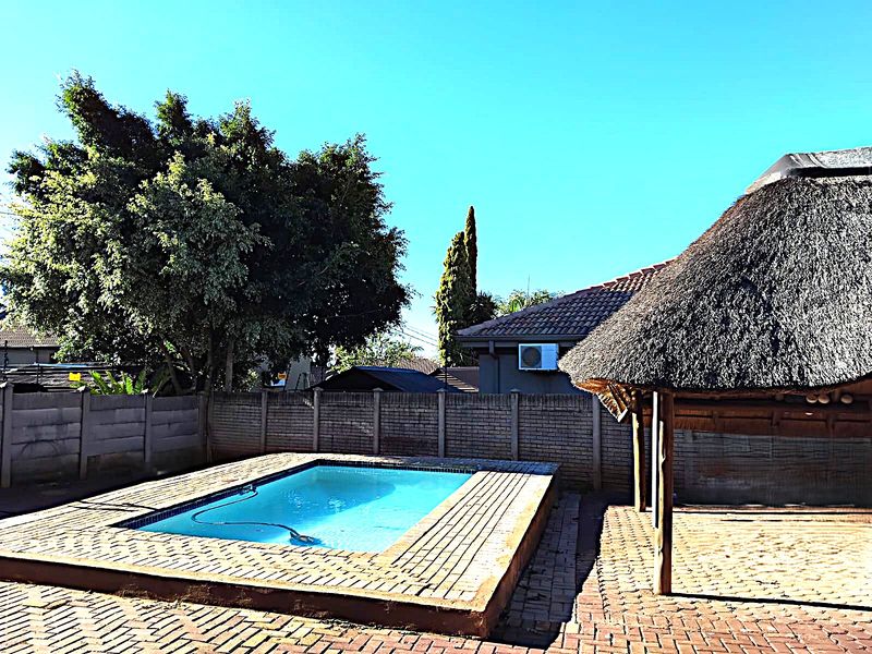 Outdoor entertainment area featuring a swimming pool, paved surround, and a traditional thatch lapa structure set within a private walled garden.