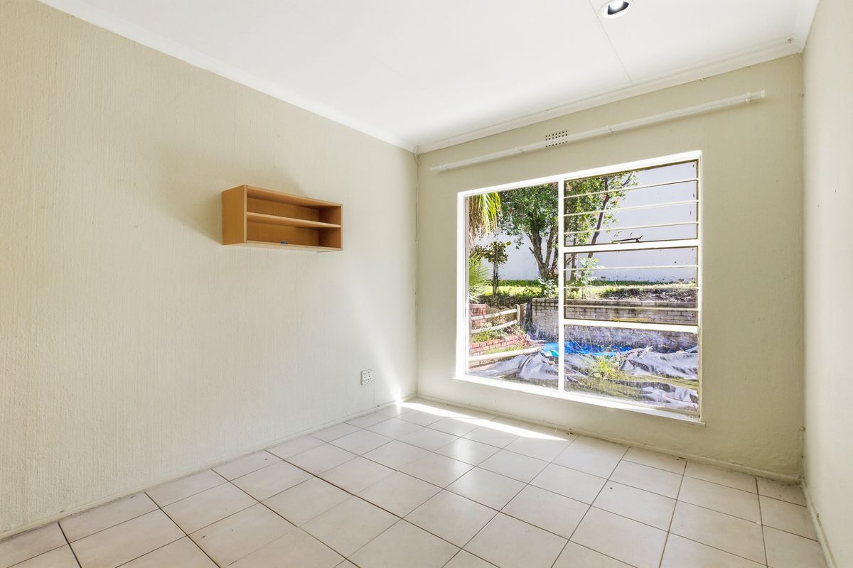 A bright, empty bedroom featuring tiled flooring, a large window with security bars, and a wall-mounted storage shelf.