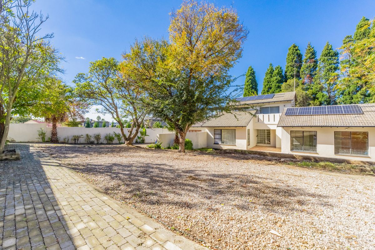Rear view of the property featuring a large gravel yard, mature trees, and solar panels installed on the tiled roof.