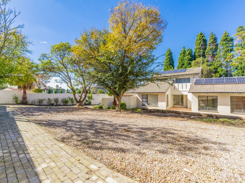 Rear view of the property featuring a large gravel yard, mature trees, and solar panels installed on the tiled roof.