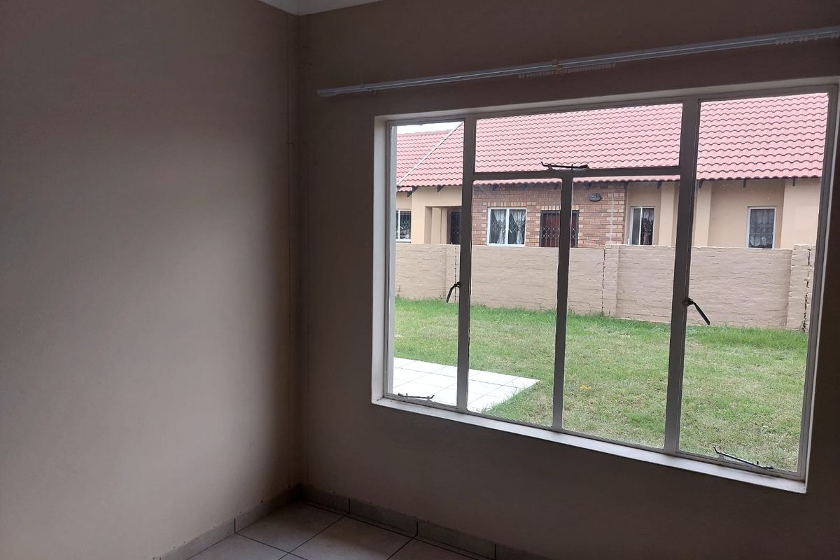 An empty bedroom featuring tiled flooring and a large window overlooking the rear garden area.
