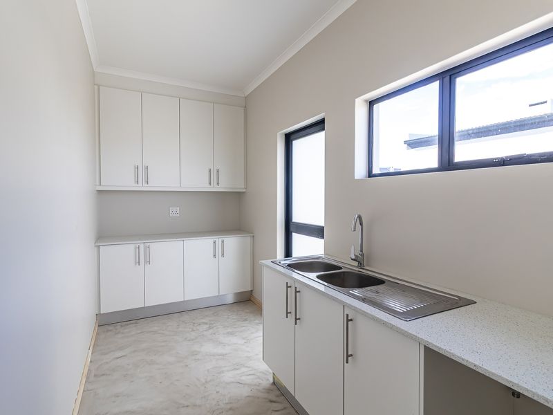 A clean, modern scullery featuring white built-in cabinetry, a double bowl sink with mixer tap, and stone-look countertops.