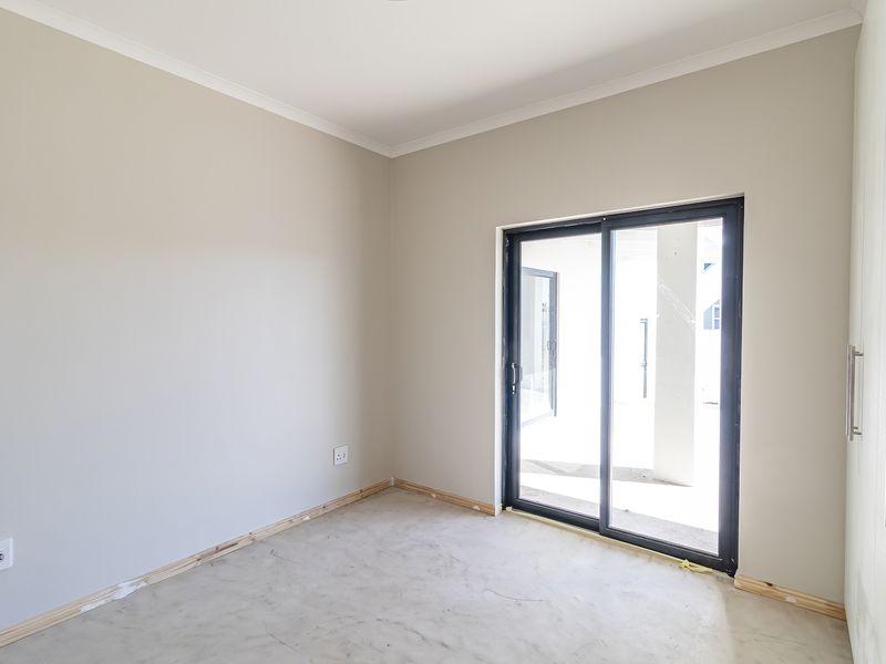 An empty bedroom featuring neutral walls, a built-in wardrobe, and a sliding glass door leading to an outdoor area, awaiting final flooring installation.