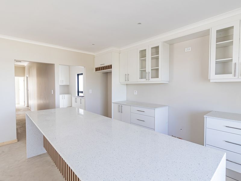A modern, bright kitchen featuring a large island with quartz countertops, ample white cabinetry, and clean finishes in a newly completed space.