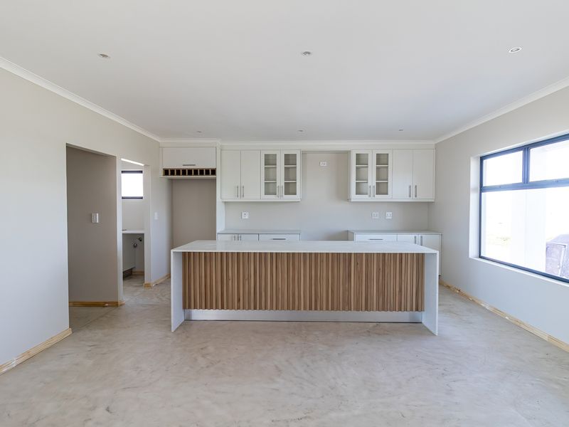 Modern kitchen featuring a central island with slatted wood detailing, white cabinetry, and stone countertops, currently awaiting final flooring installation.