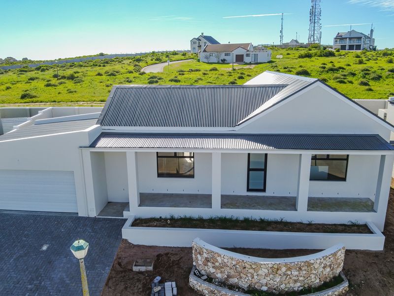 Aerial view of a modern single-story house featuring a corrugated metal roof, paved driveway, double garage, and a covered patio with a stone feature wall.