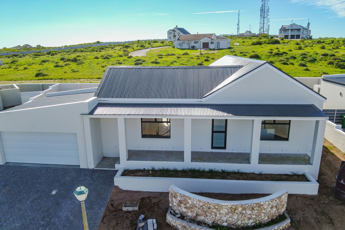 Aerial view of a modern single-story house featuring a corrugated metal roof, paved driveway, double garage, and a covered patio with a stone feature wall.