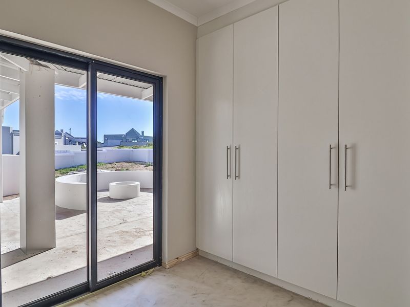 A bright, empty bedroom featuring built-in white cupboards and a sliding glass door providing direct access to an outdoor patio area.