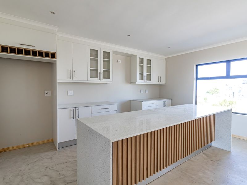 Modern kitchen featuring white cabinetry, stone countertops, and a timber-accented island, awaiting final appliance installation and flooring completion.