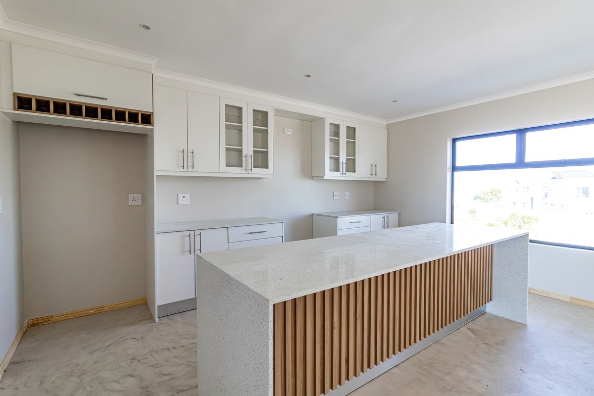 Modern kitchen featuring white cabinetry, stone countertops, and a timber-accented island, awaiting final appliance installation and flooring completion.