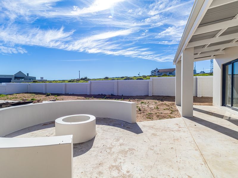 Outdoor patio area featuring a built-in fire pit, curved masonry seating, and a covered section, overlooking an expansive, unfinished backyard space.