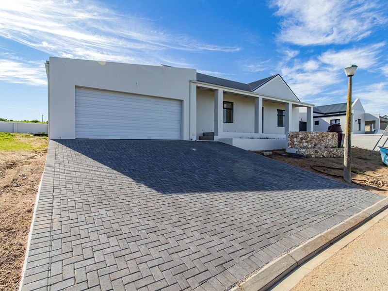 Modern single-story house featuring a paved driveway, double garage, and a covered entrance porch with stone cladding detail.
