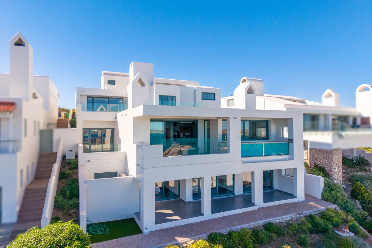 A modern multi-level residential property featuring white exterior walls, expansive glass sliding doors, glass balustrades, and tiered patio areas.