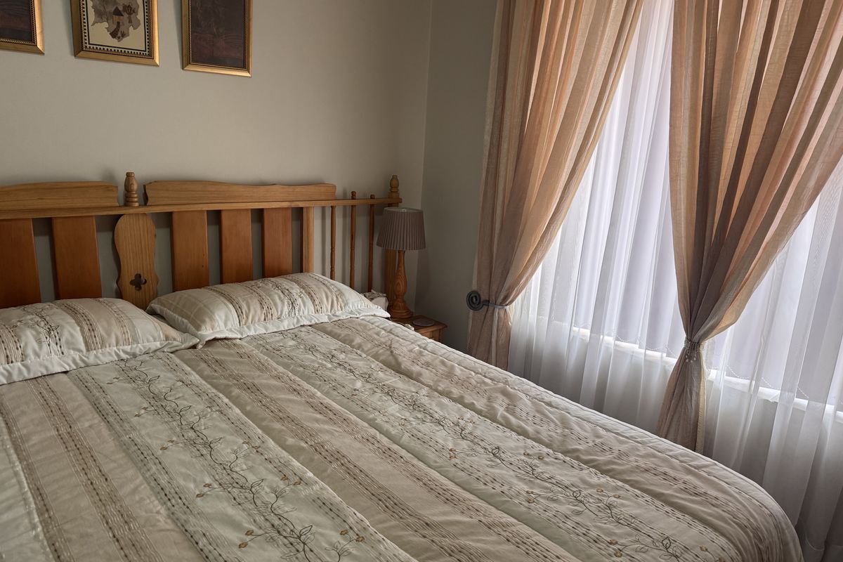 A cozy bedroom featuring neutral wall tones and natural light filtered through layered curtains.