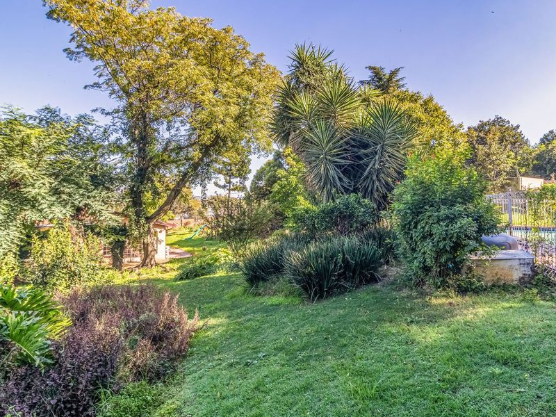 A spacious, well-established garden featuring mature trees, lush lawn, and secure pool fencing, offering a private outdoor setting.