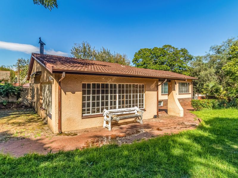 Rear view of the house featuring a tiled roof, stucco facade, steel frame windows, and a brick-paved patio area overlooking the garden.