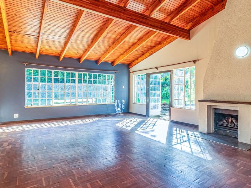 Spacious living room featuring a high exposed timber beam ceiling, classic parquet flooring, and a built-in fireplace with direct access to the garden.