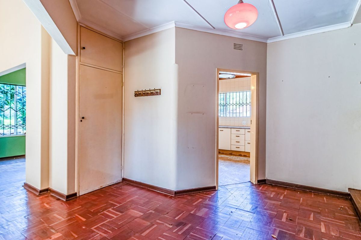 An empty living area featuring original parquet flooring and a built-in storage cupboard, with a view through to the kitchen area.
