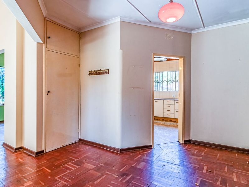 An empty living area featuring original parquet flooring and a built-in storage cupboard, with a view through to the kitchen area.