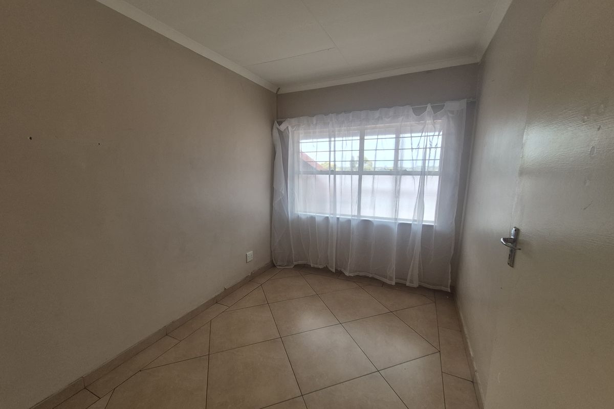 An empty bedroom featuring tiled flooring, neutral walls, and a window fitted with security bars.