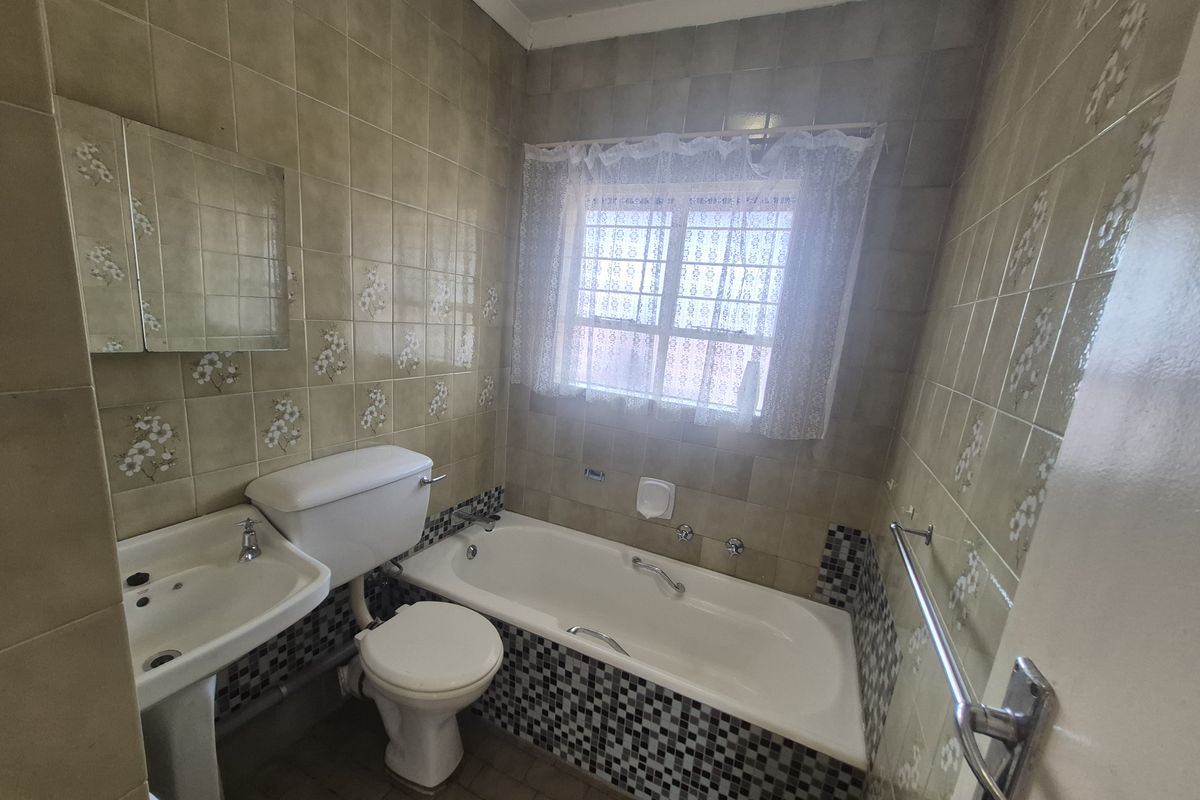 A dated bathroom featuring a pedestal basin, toilet, and bathtub with decorative wall and floor tiling.