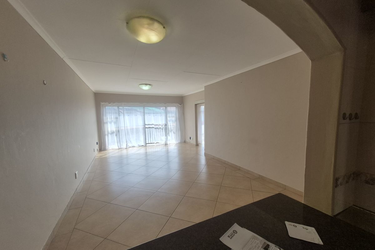 An empty, open-plan living area featuring neutral walls, tiled flooring, and a sliding glass door providing natural light.