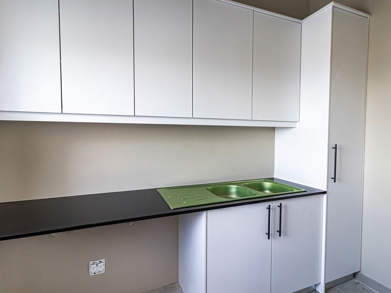 A clean, modern scullery area featuring white built-in cabinetry, a black laminate countertop, and a stainless steel sink.