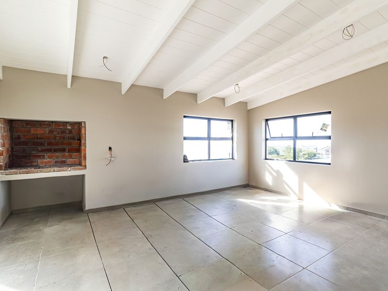 Spacious living area featuring exposed beam ceilings, tiled flooring, and a built-in brick fireplace, offering a blank canvas for interior design.