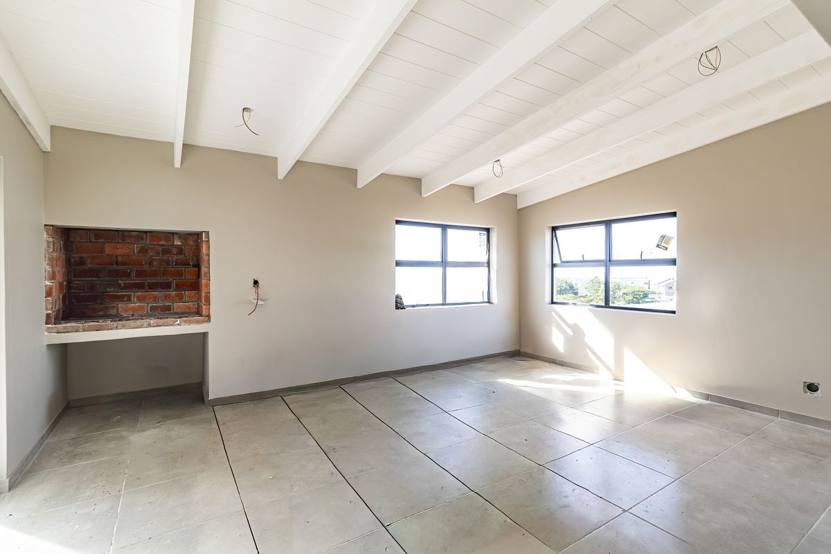 Spacious living area featuring exposed beam ceilings, tiled flooring, and a built-in brick fireplace, offering a blank canvas for interior design.