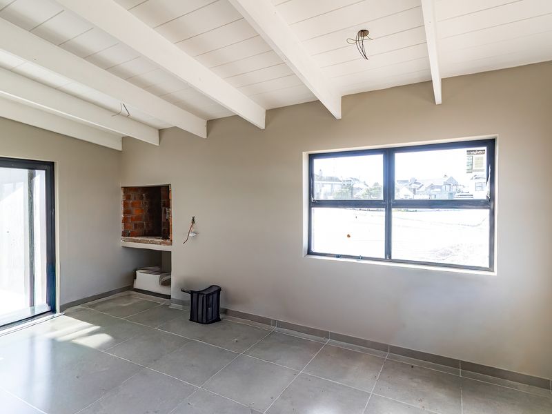 An empty living room featuring exposed white beams, tiled flooring, a built-in fireplace, and large windows providing natural light.