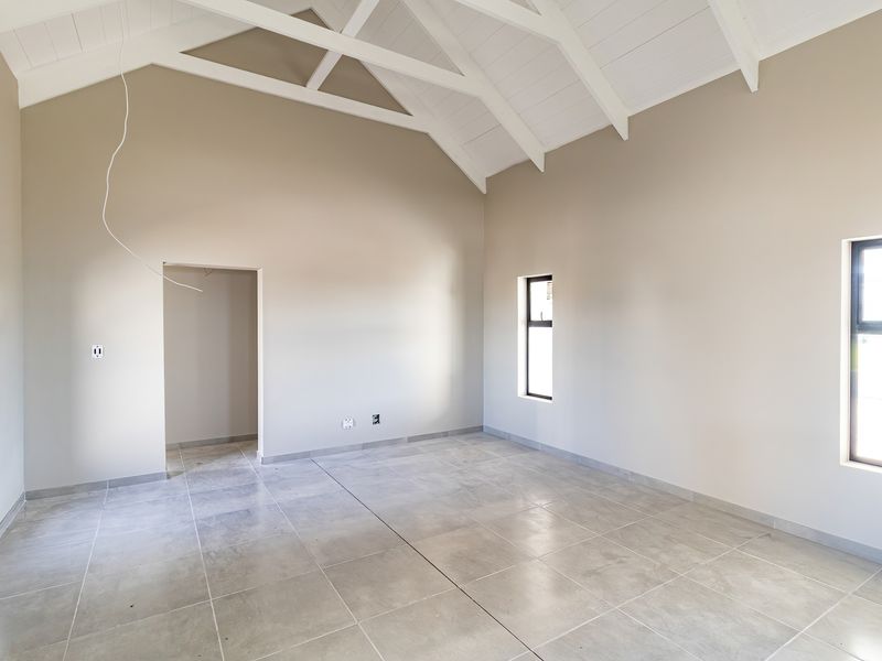 Spacious living area featuring a high vaulted ceiling with exposed white timber trusses and neutral tiled flooring, offering a bright and modern blank canvas.
