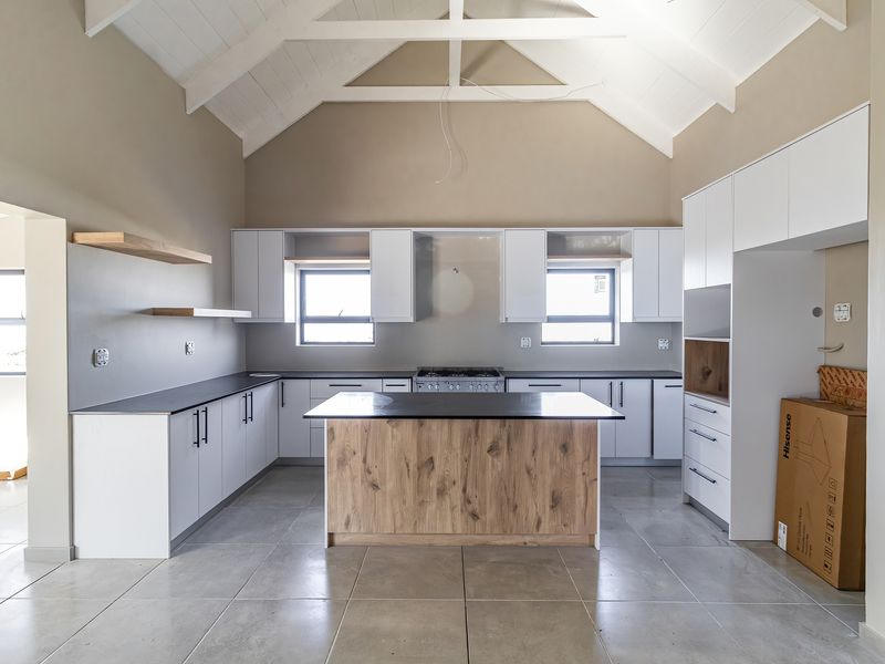 Modern kitchen featuring a central island, white cabinetry, stone countertops, gas stove, and high vaulted ceilings with exposed timber trusses.