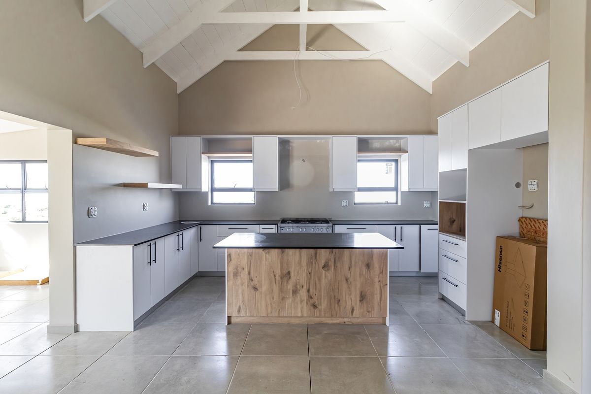 Modern kitchen featuring a central island, white cabinetry, stone countertops, gas stove, and high vaulted ceilings with exposed timber trusses.