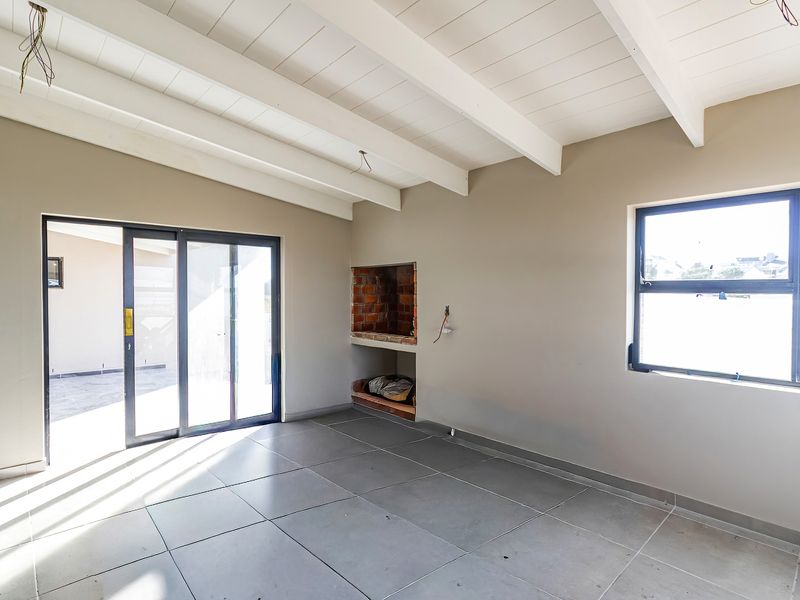 An empty living room featuring exposed beam ceilings, tiled flooring, a built-in fireplace, and sliding glass doors leading to an outdoor area.