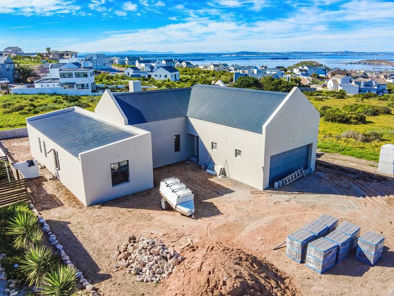 Aerial view of a modern, newly constructed house with a metal roof, featuring an attached garage and surrounding coastal landscape.
