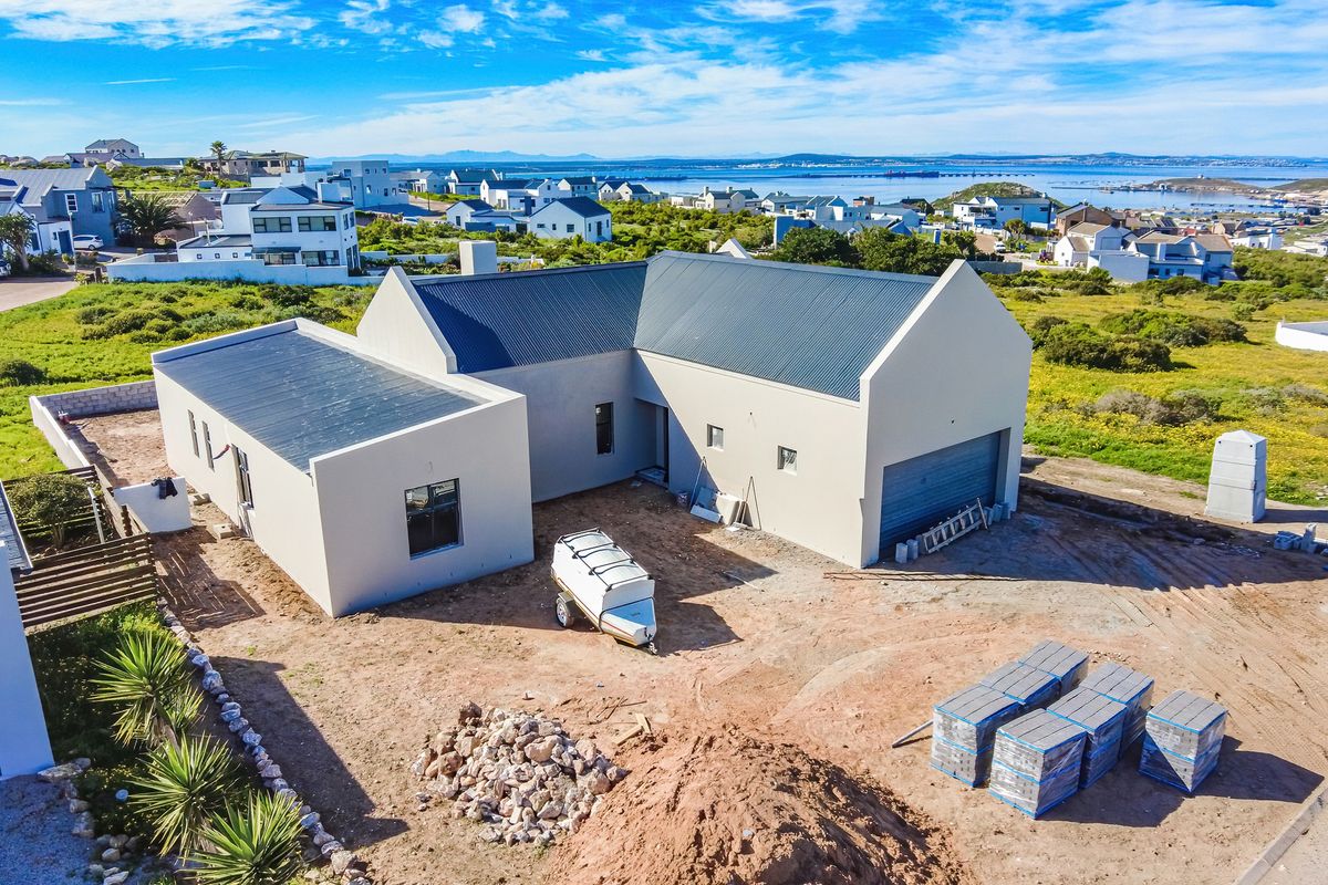 Aerial view of a modern, newly constructed house with a metal roof, featuring an attached garage and surrounding coastal landscape.