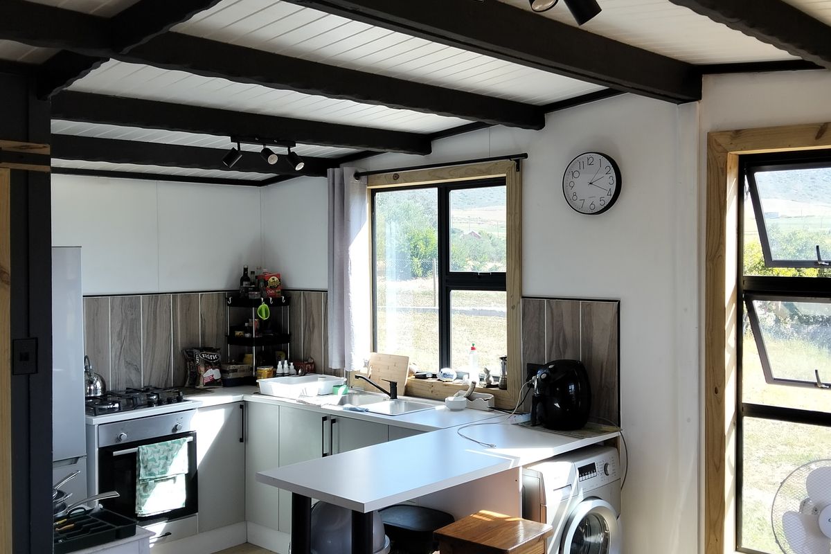 A functional kitchen featuring a gas hob, built-in oven, tiled splashback, and exposed timber ceiling beams, with ample natural light from large aluminium windows.
