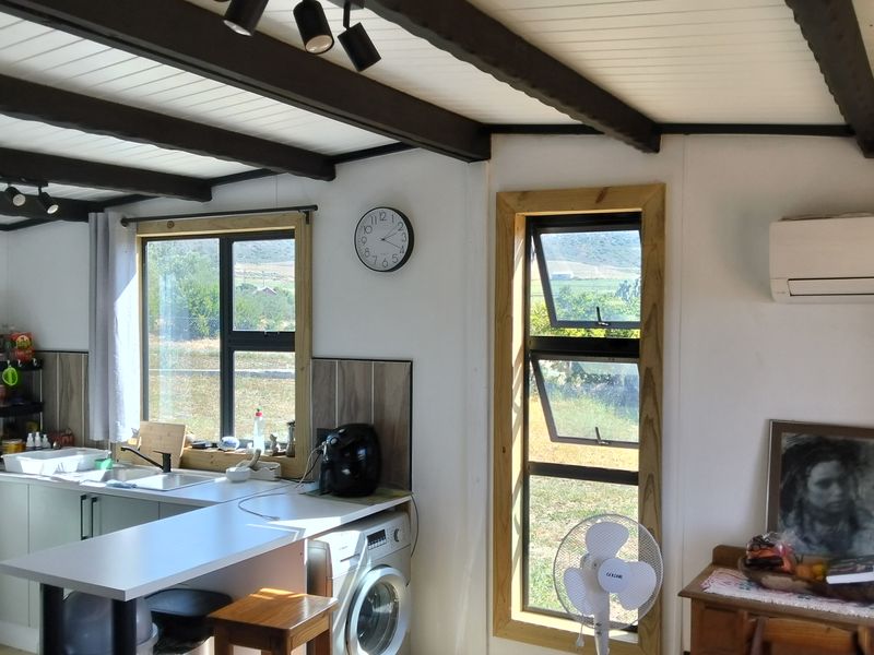 Open-plan kitchen area featuring exposed timber ceiling beams, track lighting, built-in cabinetry, and integrated laundry facilities with views of the surrounding landscape.