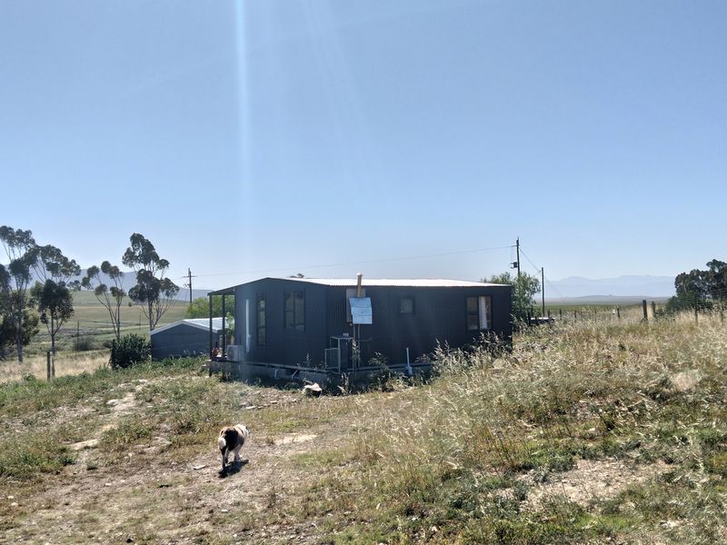 A detached structure with corrugated metal cladding and a metal roof, situated on a rural plot with natural vegetation.