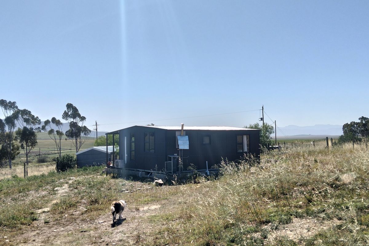 A detached structure with corrugated metal cladding and a metal roof, situated on a rural plot with natural vegetation.